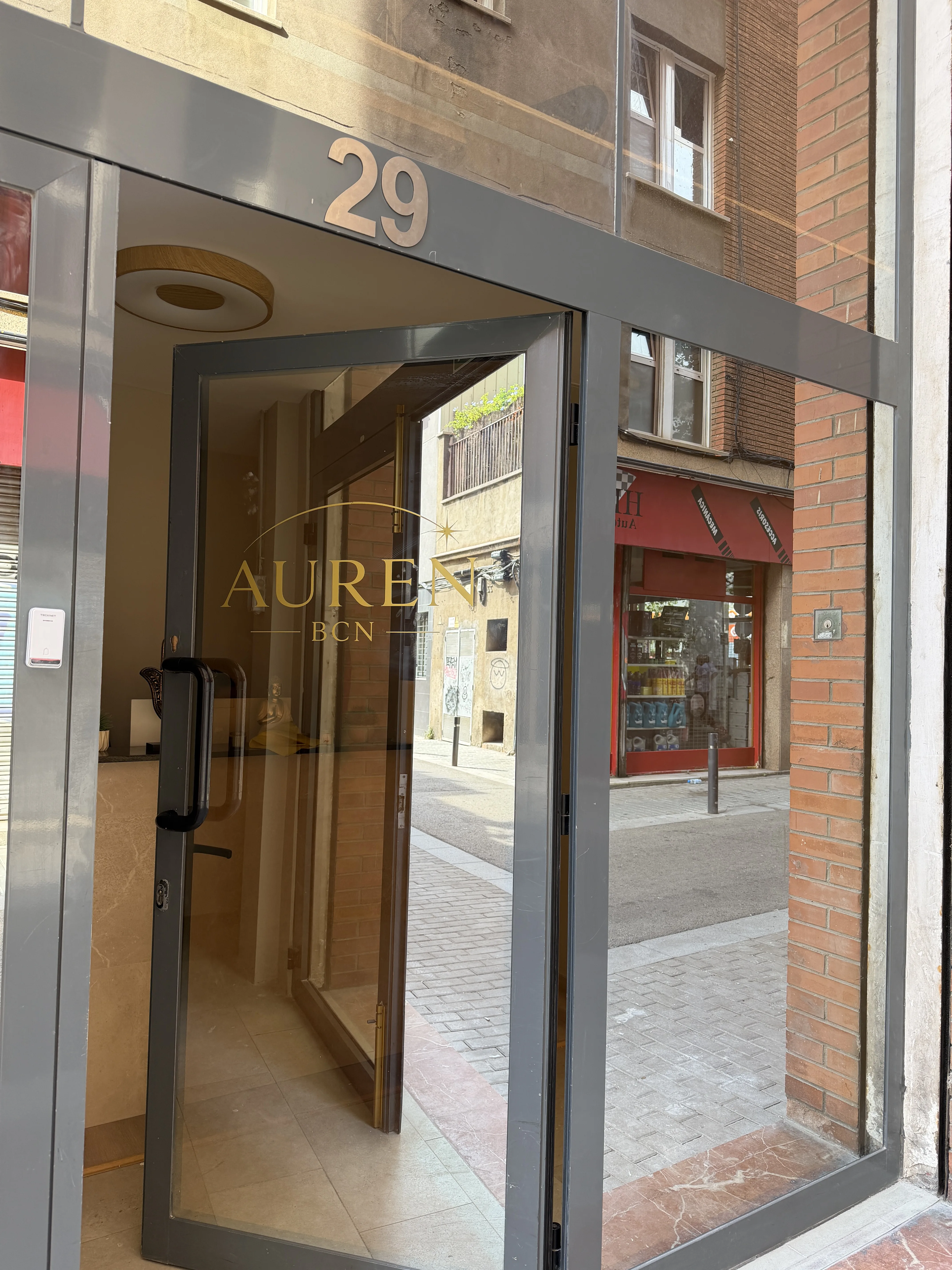 Puerta abierta de Auren BCN con el número 29 sobre el marco y el vinilo dorado en el cristal