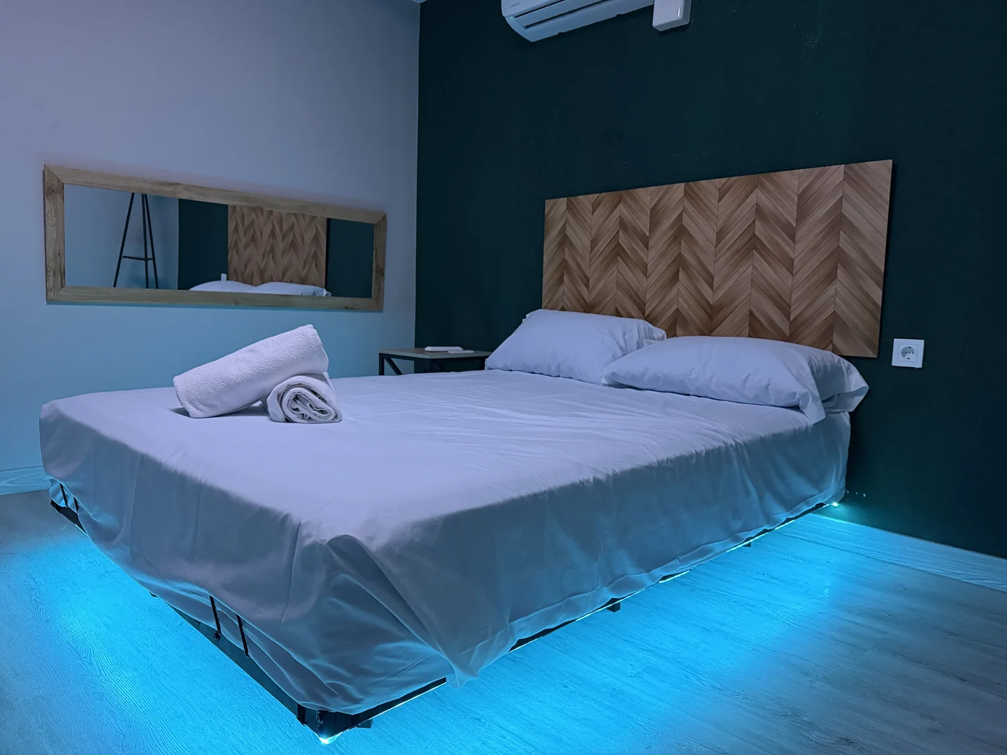 Sala con textiles blancos, pared verde y luz azul bajo la cama