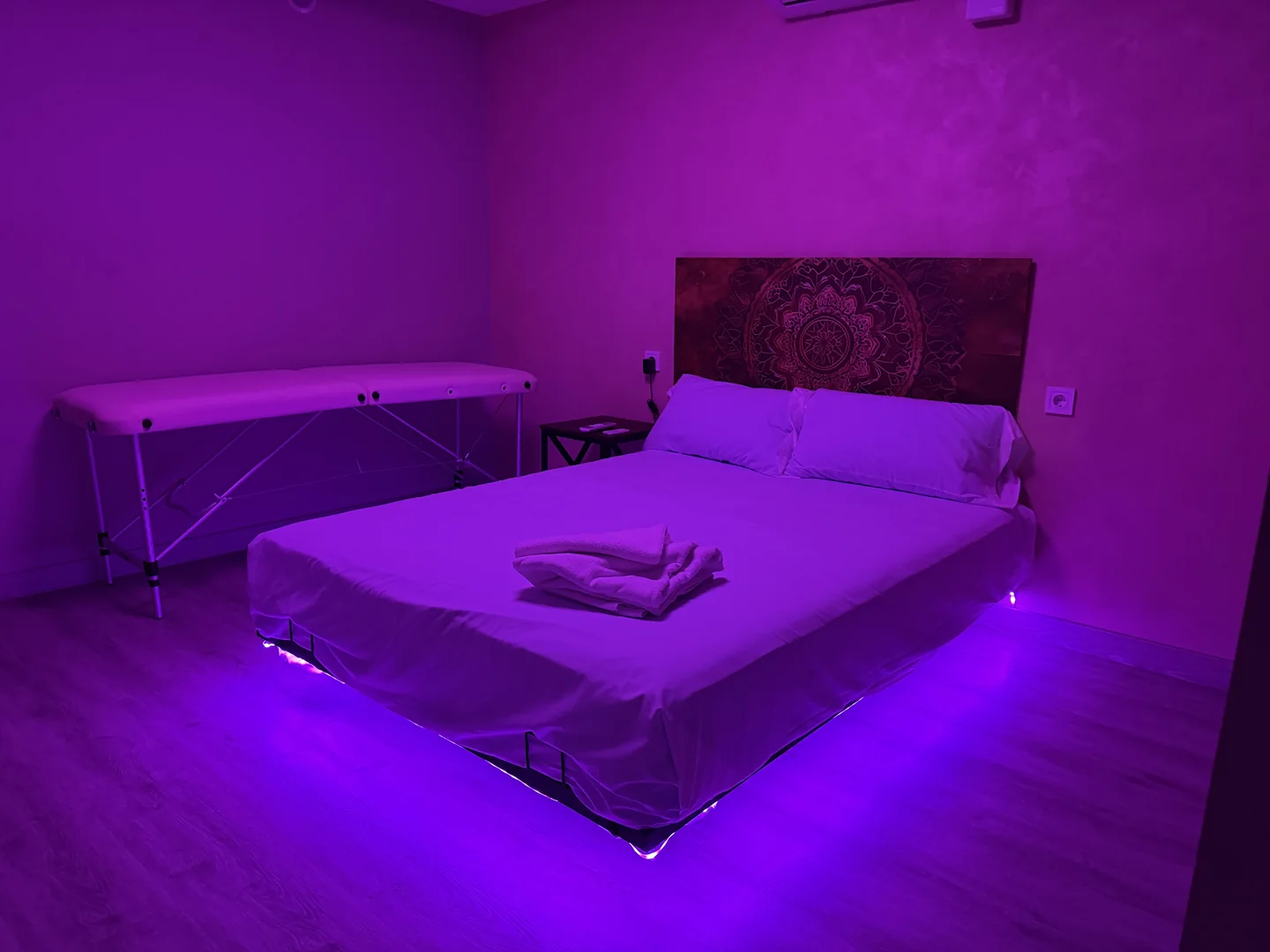 Sala con iluminación violeta, textiles blancos y camilla junto a la pared