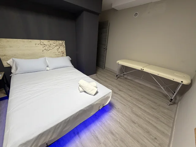 Sala con textiles blancos, iluminación azul y camilla junto a la pared